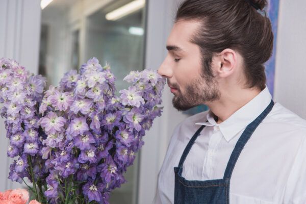 Ragazzo con i capelli lunghi e il grembiule da barbiere che annusa fiori viola.