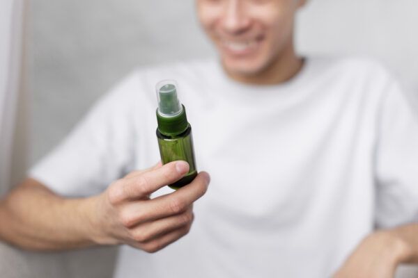 Uomo sorridente in camicia bianca che tiene in mano un flacone spray verde.