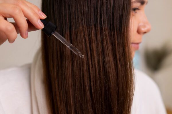 Ragazza dai capelli castani che applica l'olio di cocco sui capelli con un erogatore.