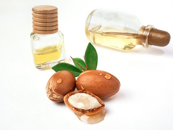 Tre noci di argan con foglie verdi in bottiglie di vetro su sfondo bianco isolato