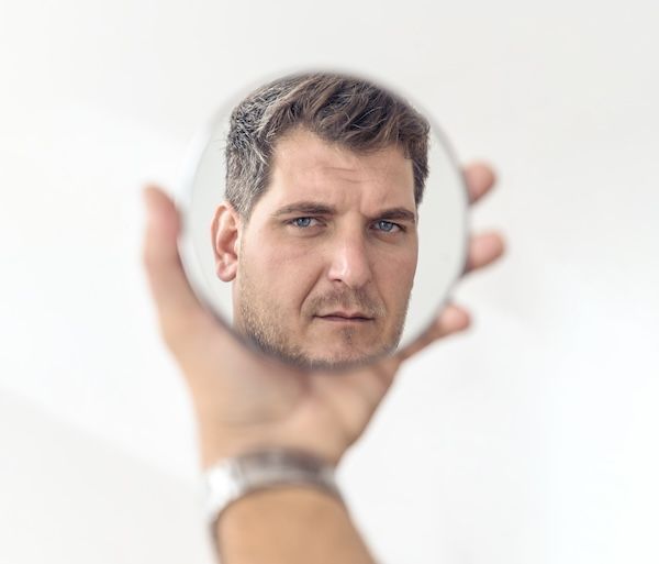 uomo adulto che si guarda allo specchio che tiene in mano