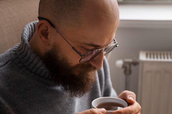 uomo calvo con barba e occhiali che guarda la sua tazza di caffè