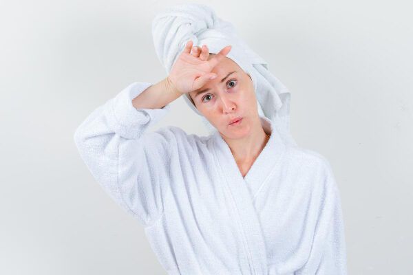donna caucasica con accappatoio e asciugamano in testa con mano sulla fronte