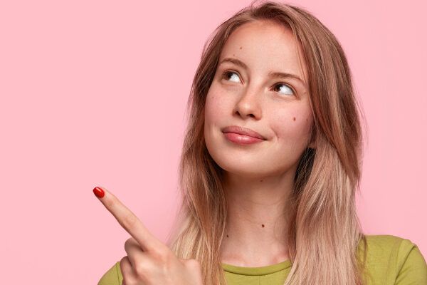 Giovane bionda con la mano rivolta verso l'alto - Giovane ragazza che sottolinea un dettaglio che ha attirato la sua attenzione. Scrivi i tuoi consigli su cosa sono gli scrub.