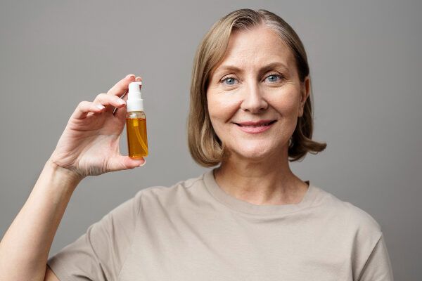 Donna anziana con i capelli grigi e un contagocce in mano - Benefici dell'olio di ricino.
