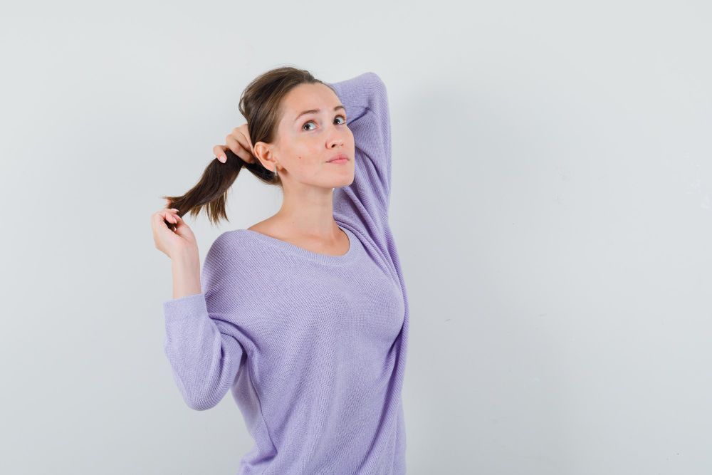 Donna in camicetta viola che tiene i capelli in una semi coda di cavallo pensando a qualcosa - Caduta dei capelli causata dal Covid.