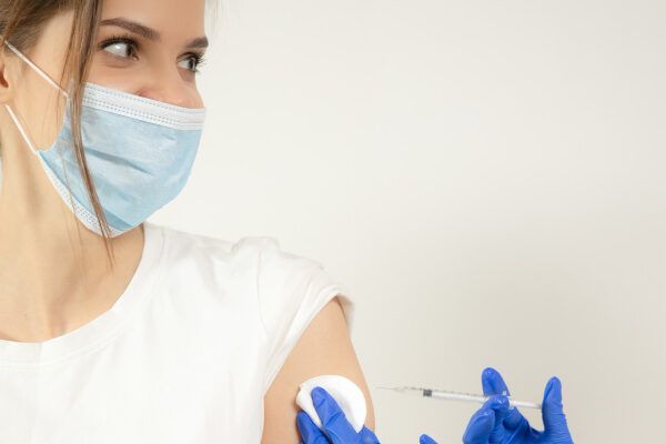Giovane uomo dai capelli castani con una maschera che riceve un vaccino.