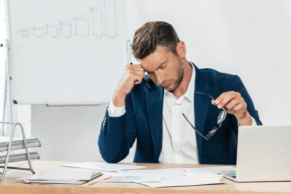 Uomo d'affari con barba e abito blu navy alla sua scrivania con espressione preoccupata.