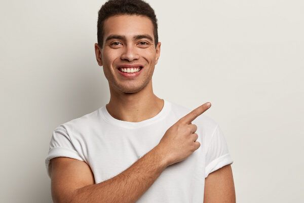 Giovane con la pelle scura e i capelli ricci che sorride e punta verso l'alto - Capelli sani dall'interno