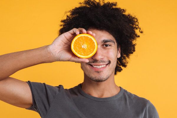 Il giovane con pelle scura e capelli afro mostra a mezza arancia con la mano mentre sorride.