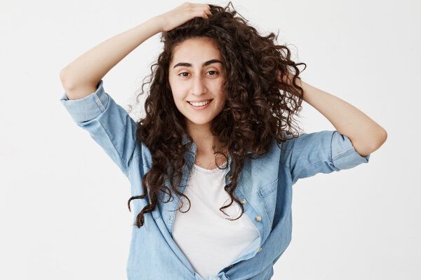 Giovane ragazza con capelli ricci castano scuro che sorride alla macchina fotografica mentre la accarezza delicatamente.