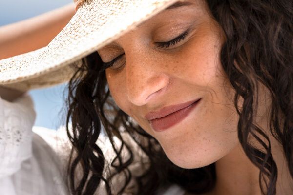 Giovane donna dalla carnagione chiara con lentiggini che proteggono i capelli e la pelle del viso dai raggi del sole.