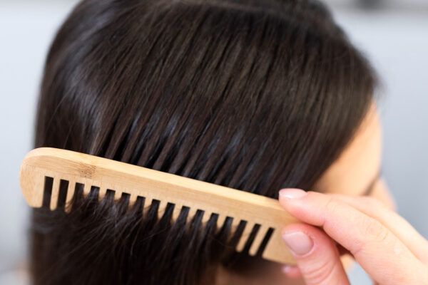 Donna che si spazzola i capelli dalle radici con un pettine di legno con setole separate.