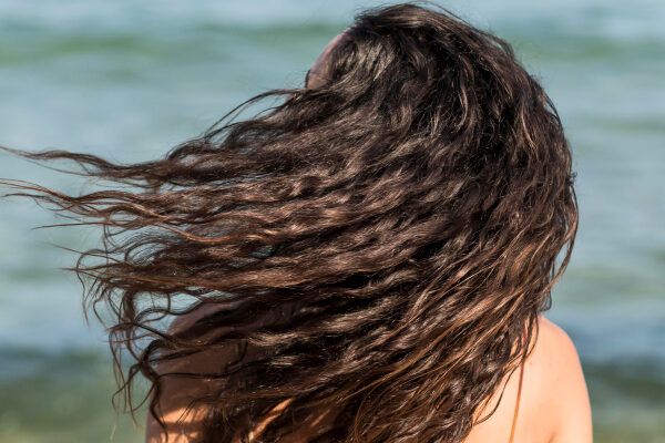 Donna con riccioli che scuotono i capelli sulla riva della spiaggia - Sole danneggia i capelli