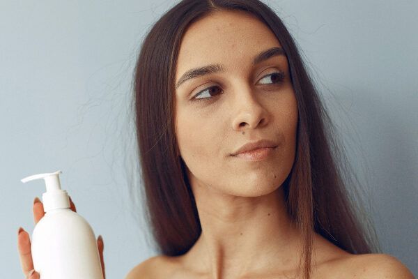 Donna dalla pelle scura con uno shampoo in mano in posa per la macchina fotografica mentre mostra il suo profilo.