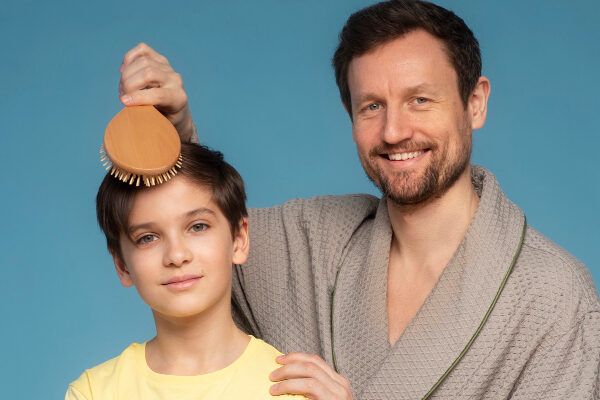 Giovane padre in accappatoio che pettina i capelli di suo figlio - Alopecia nei giovani.