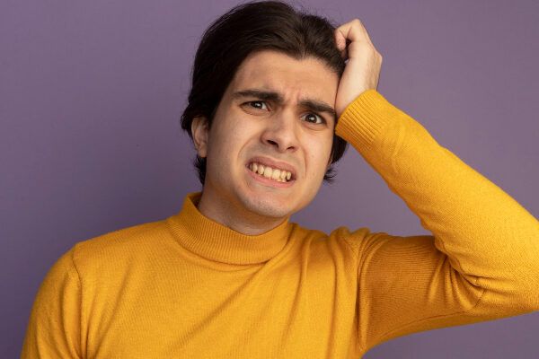 Giovane uomo in maglione a maniche lunghe color senape con capelli lunghi ed espressione di preoccupazione per qualche situazione difficile.