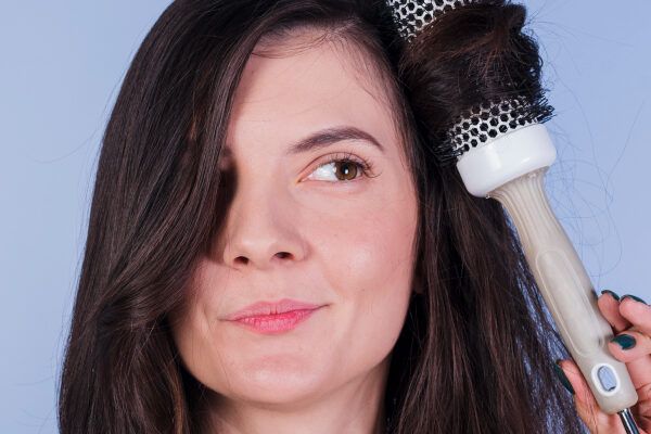 Donna con una spazzola rotonda per asciugare i capelli tra le mani che si pettina i capelli mentre guarda in diagonale - Acconciature da evitare.