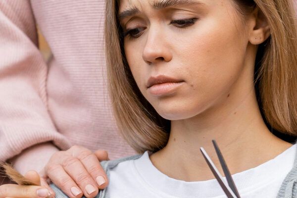 Ragazza con i capelli biondi tinti seduta al parrucchiere mentre tiene i capelli tagliati tra le mani con un'espressione triste e preoccupata.