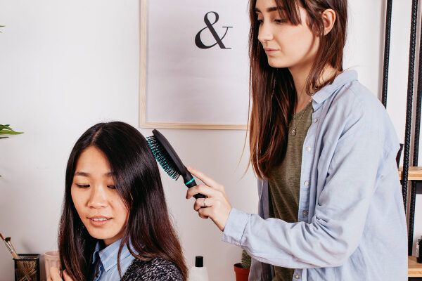 Ragazza che pettina i capelli lisci di una giovane donna asiatica con una spazzola cellulare.
