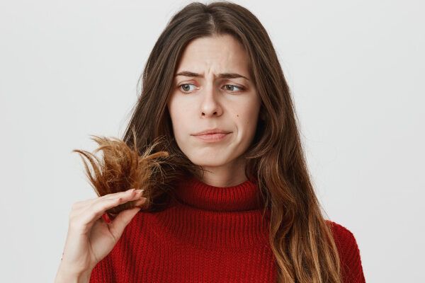 Giovane ragazza con un maglione rosso e capelli lunghi che guarda le estremità dei suoi capelli con espressione preoccupata - Effetto shedding.