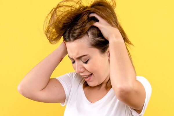Giovane donna con capelli castani corti che agita il cuoio capelluto con un'espressione di shock e stress.