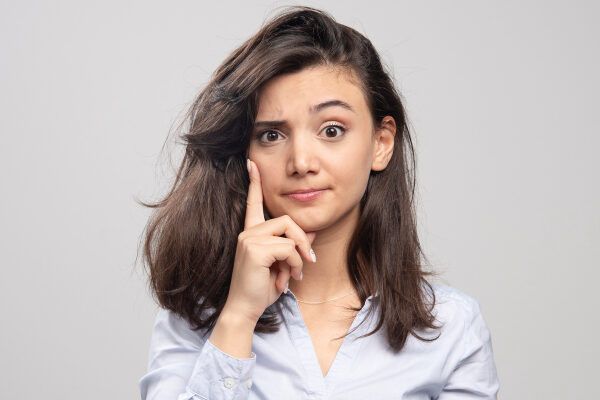 Giovane ragazza con i capelli corti con una camicia grigia che si tocca la guancia in un'espressione di dubbio riguardo a una situazione - Effetto shedding.
