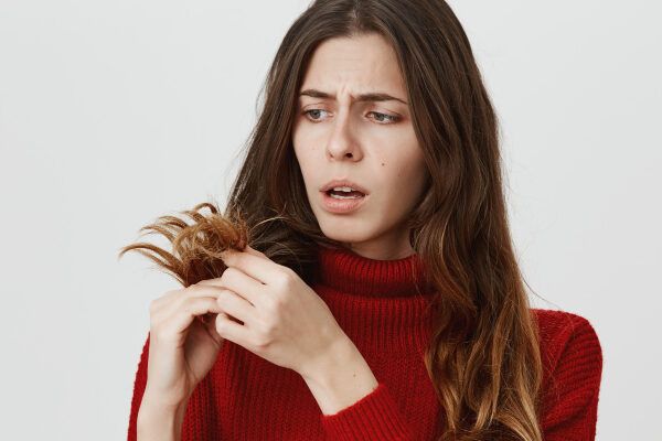 Giovane donna con lunghi capelli castano chiaro che guarda le sue doppie punte secche con un'espressione preoccupata - Vegetariani fa perdere i capelli.