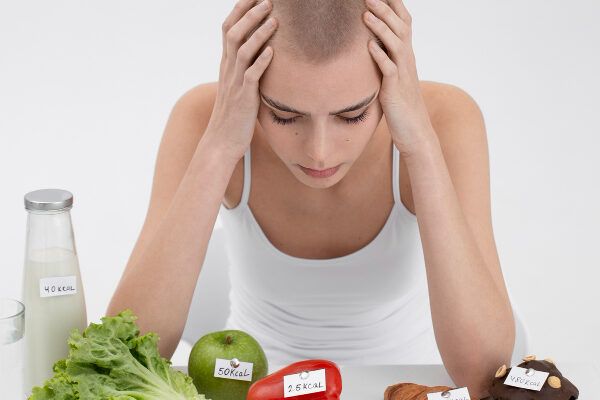 Ragazza giovane con l'espressione angosciata che guarda un tavolo pieno di verdure e cibo.