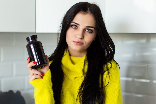 Donna dagli occhi chiari con un maglione e vitamine in mano.