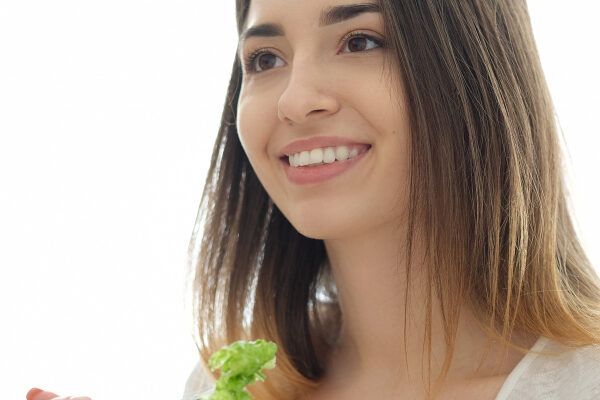 Ragazza sorridente con capelli sani e nutriti mentre mangia insalata - Vegetariani fa perdere i capelli.