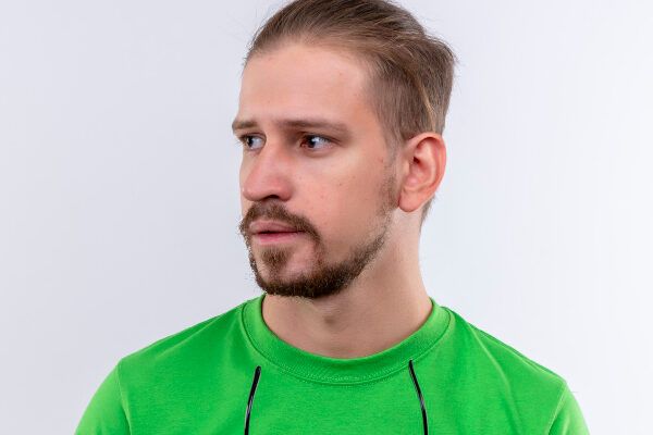Giovane con i capelli corti e flanella verde che guarda di lato con espressione sorpresa e occhiali da sole in mano.