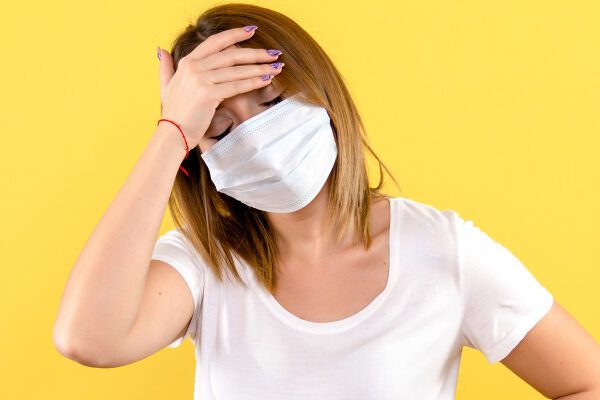 Donna con maschera che si tocca la fronte preoccupata - Linquinamento influisce sulla caduta.