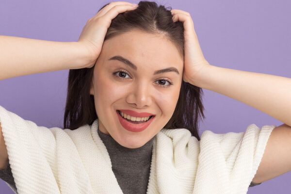 Giovane ragazza dalla carnagione chiara che si tocca il cuoio capelluto con entrambe le mani mentre sorride alla telecamera.