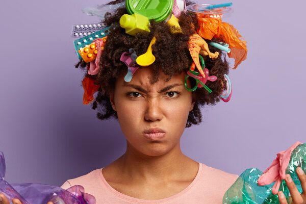 Donna dalla pelle scura che guarda la telecamera accigliata perché i suoi capelli sono pieni di plastica - Linquinamento influisce sulla caduta.