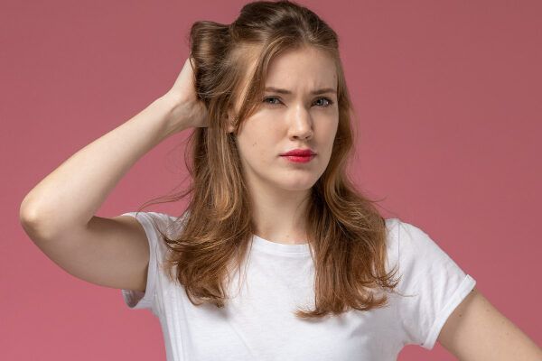 Ragazza giovane con capelli castano chiaro con espressione confusa mentre si tocca il cuoio capelluto - Laser per capelli.