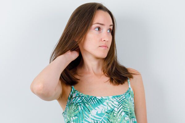 Donna di mezza età in flanella tropicale con capelli lunghi fino alle spalle che le accarezzavano il collo dubbiosamente mentre guardava di lato - Laser per capelli.