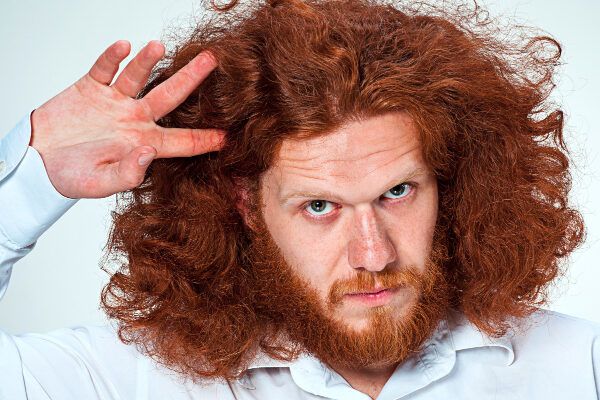 Uomo dai capelli rossi che si tocca i bigodini mentre guarda la telecamera con un'espressione sobria - Sindrome dei capelli impettinabili.