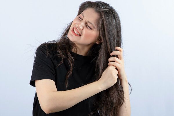 Donna con capelli fini e riccioli castano scuro che tirano le punte con un'espressione lamentosa - Tricoressi nodosa.