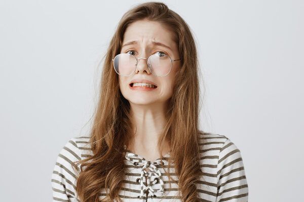 Giovane ragazza con occhiali adattati con capelli castani e riccioli fini alle estremità con un'espressione di dubbio o paura - Tricoressi nodosa.