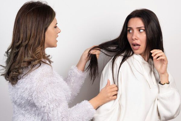 Donna che controlla le estremità dei capelli della sua amica che ha un'espressione sorpresa.