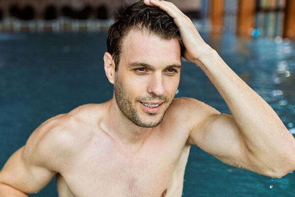 Giovane che fa il bagno in piscina sorridendo mentre si pettina i capelli.