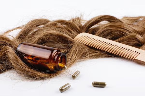 pettine di legno bottiglia e vitamine accanto a riccioli castani