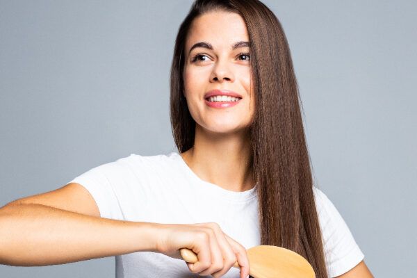 Giovane ragazza che si pettina i lucenti capelli castani con una spazzola cellulare e sorride in grande - Capelli: Che c'è da sapere.