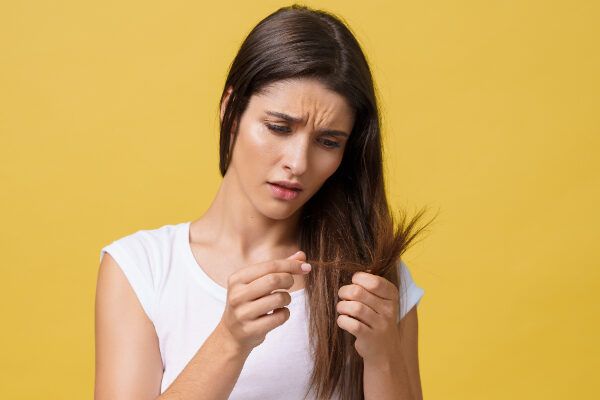 Giovane ragazza che guarda e tocca le estremità dei suoi capelli preoccupata.