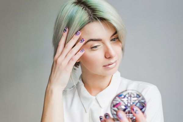 Donna con i capelli verde acqua sbiaditi che si guarda allo specchio mentre si tocca le punte dei capelli.