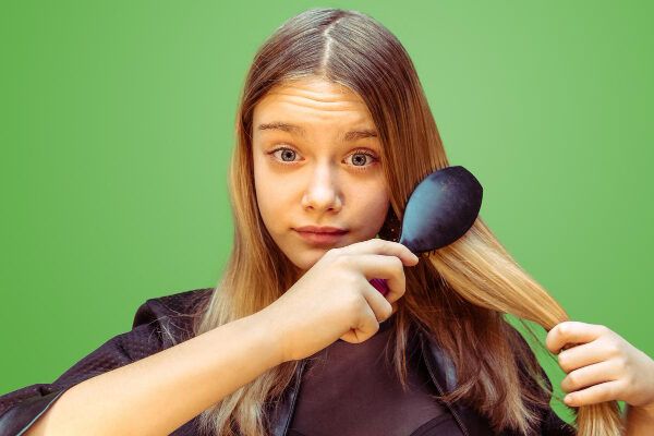 Giovane ragazza con gli occhi chiari che guarda la telecamera con un'espressione sorpresa mentre si pettina i capelli lisci.