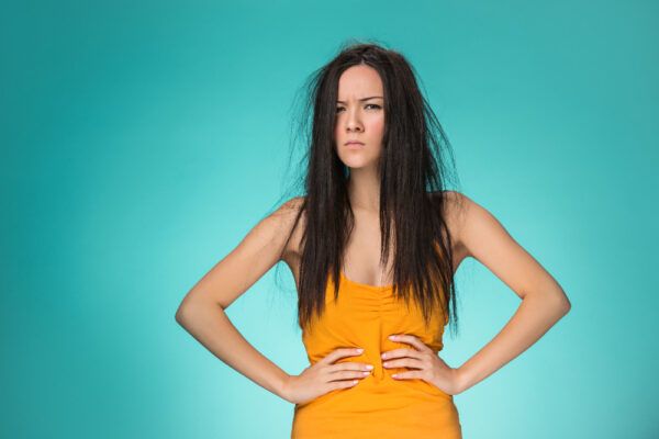 Ragazza con capelli neri lunghi, arruffati e asciutti con un'espressione lamentosa che guarda la telecamera - Recuperare i capelli bruciati.