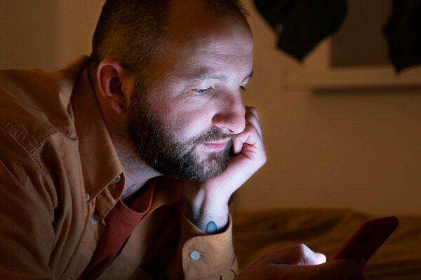 Uomo calvo che usa il telefono in una stanza buia.