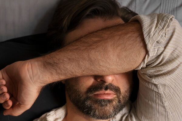 Uomo barbuto di mezza età che si copre gli occhi con l'avambraccio mentre è sdraiato.